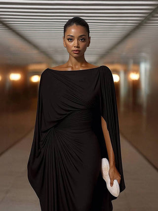 Robe maxi noire à taille drapée, encolure bateau, manches cape tombantes, coupe longue.