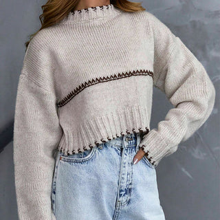 Pull court en tricot gris clair avec rayure contrastée, manches longues et bord effiloché.