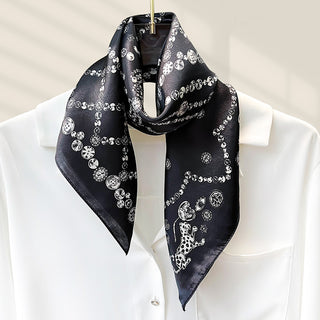 Foulard carré en soie noir à motifs médaillons blancs, noué au cou.
