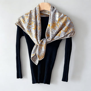 Grand foulard double face imprimé jungle beige et gris, noué sur le cou.