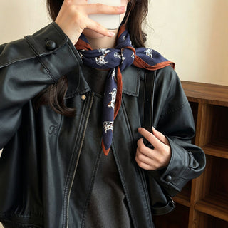 Foulard en soie imprimé chevaux, fond bleu marine sombre, bord orange, noué.