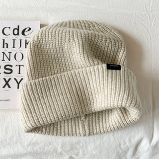 Bonnet en laine crème, maille côtelée, revers large, étiquette noire discrète