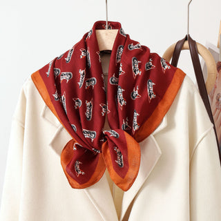 Foulard en soie imprimé chevaux, bordeaux avec bordure orange, plié en carré.