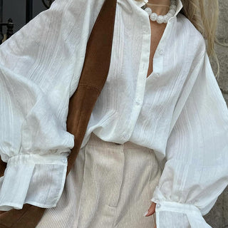 Chemise blanche boutonnée, manches volumineuses et tissu texturé, coupe ample au buste.