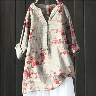 Blouse en tissu clair à fleurs rouges, col boutonné, manches retroussées.
