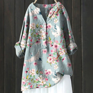 Blouse bleu ciel à fleurs roses et blanches, col boutonné, manches amples.