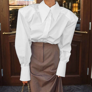 Chemise blanche à épaulettes, col pointu et poignets larges, portée rentrée dans une jupe